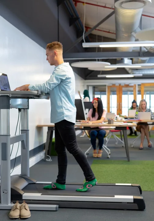 un homme qui travaille sur un ordinateur debout au bureau avec un tapis de marche